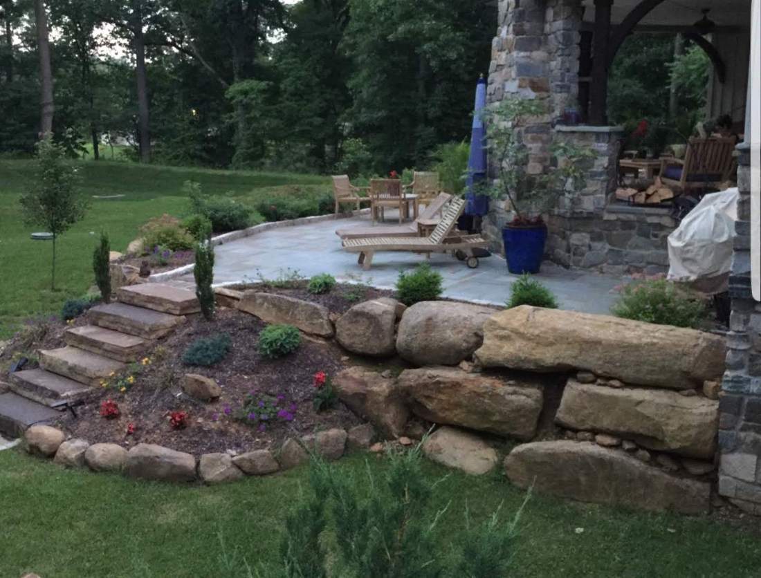 A bluestone patio and boulder retaining wall with stone steps, built by Fitzgerald Masonry in the Main Line area
