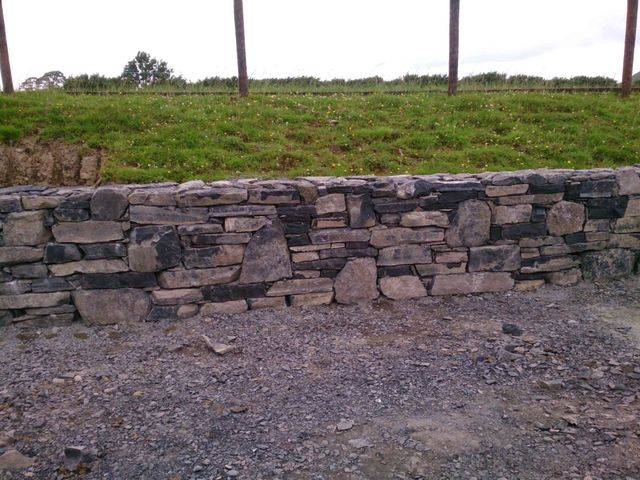 A dry-stone wall of grey and brown rocks in front of a grassy hill