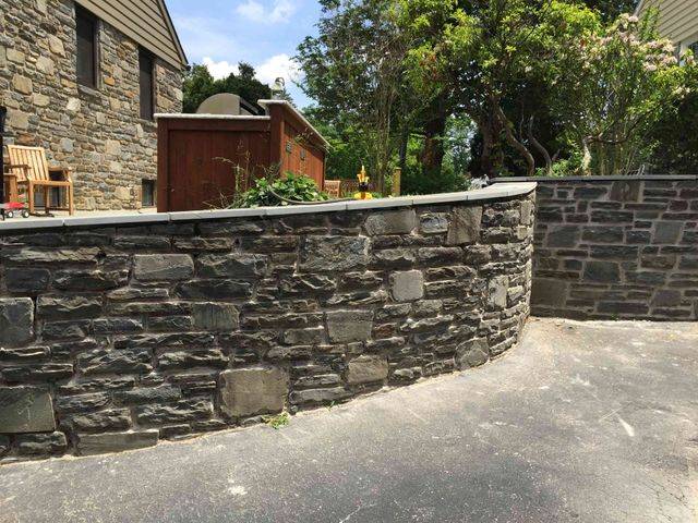 A curved stone retaining wall along an asphalt driveway beside a stone-clad house